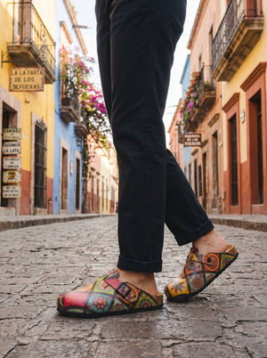 Calceo.co clogs with a colorful patchwork print, featuring a buckle strap and a cork sole. Made from artificial leather and cotton canvas.
